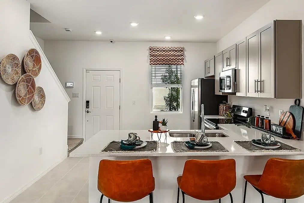 new home developments in sarasota, fl. Close to the front door and staircase is a kitchen with three orange chairs against the counter.