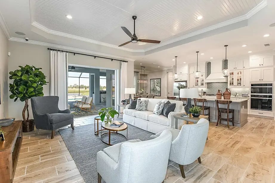 new home developments in sarasota, fl. A living room and kitchen with ceiling fan. Nearby is a sunroom with a view of the backyard.