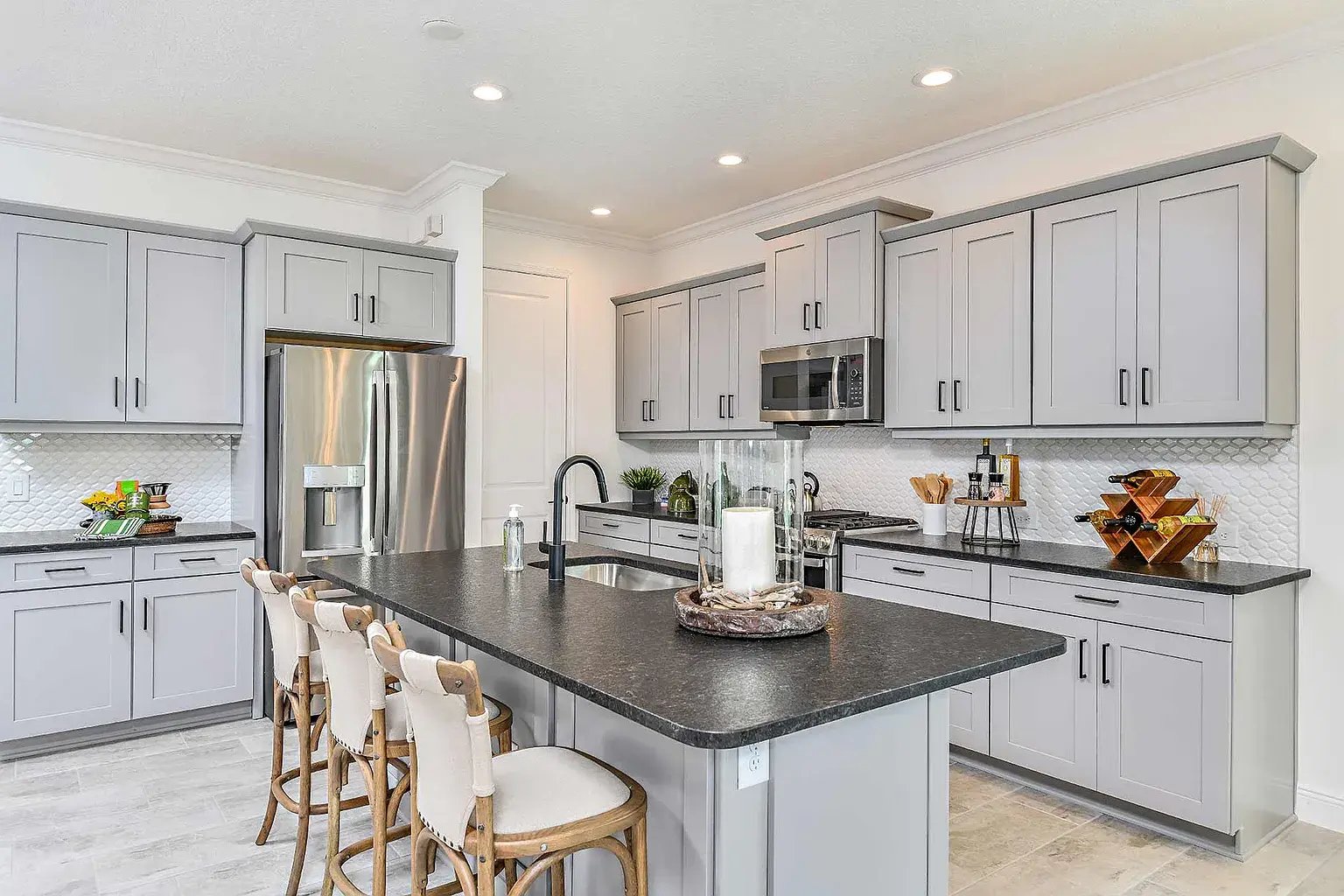 new home developments in sarasota, fl. A modern kitchen with grey cabinets and a marble island with three chairs lined up.