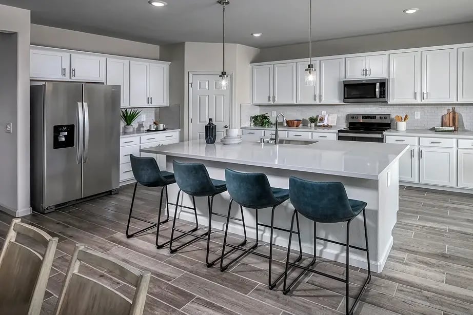 new homes in Antioch, CA. A large kitchen with four blue chairs at an island. RESIDENCE 6-Antioch, CA